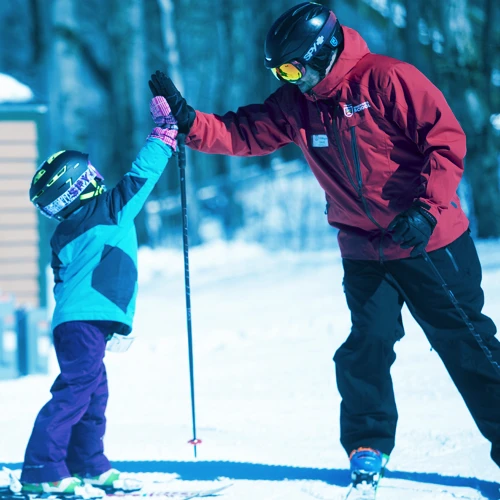 Ski school instructor high fiving lesson participant at the bottom of a trail in mid winter